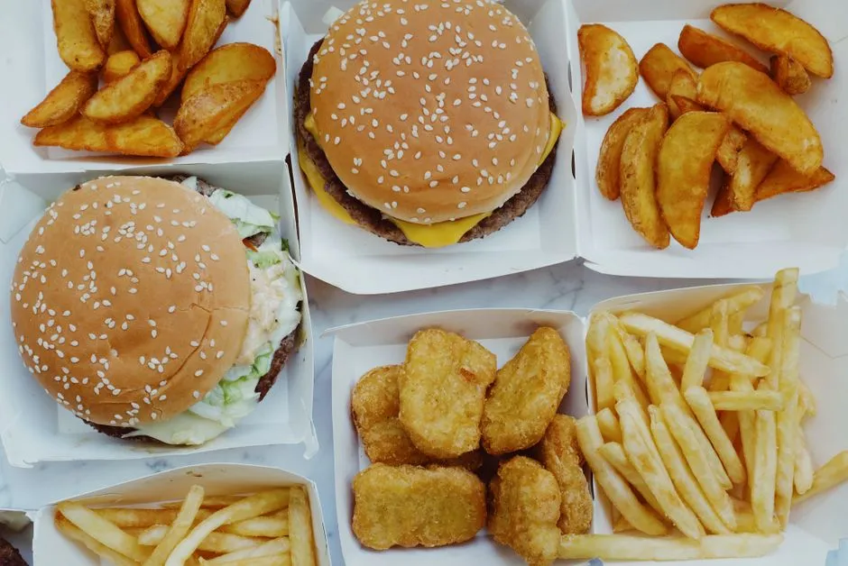 Assorted fast food combo boxes with burgers, fries, potato wedges, and chicken nuggets, illustrative photo