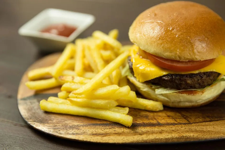 A burger and fries on a wooden board with a side of ketchup, illustrative photo